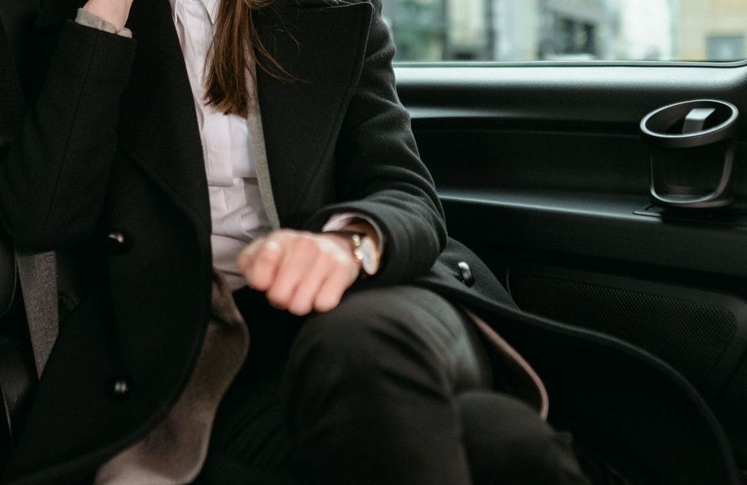 A professional woman in a blazer talks on her smartphone while seated in a car.